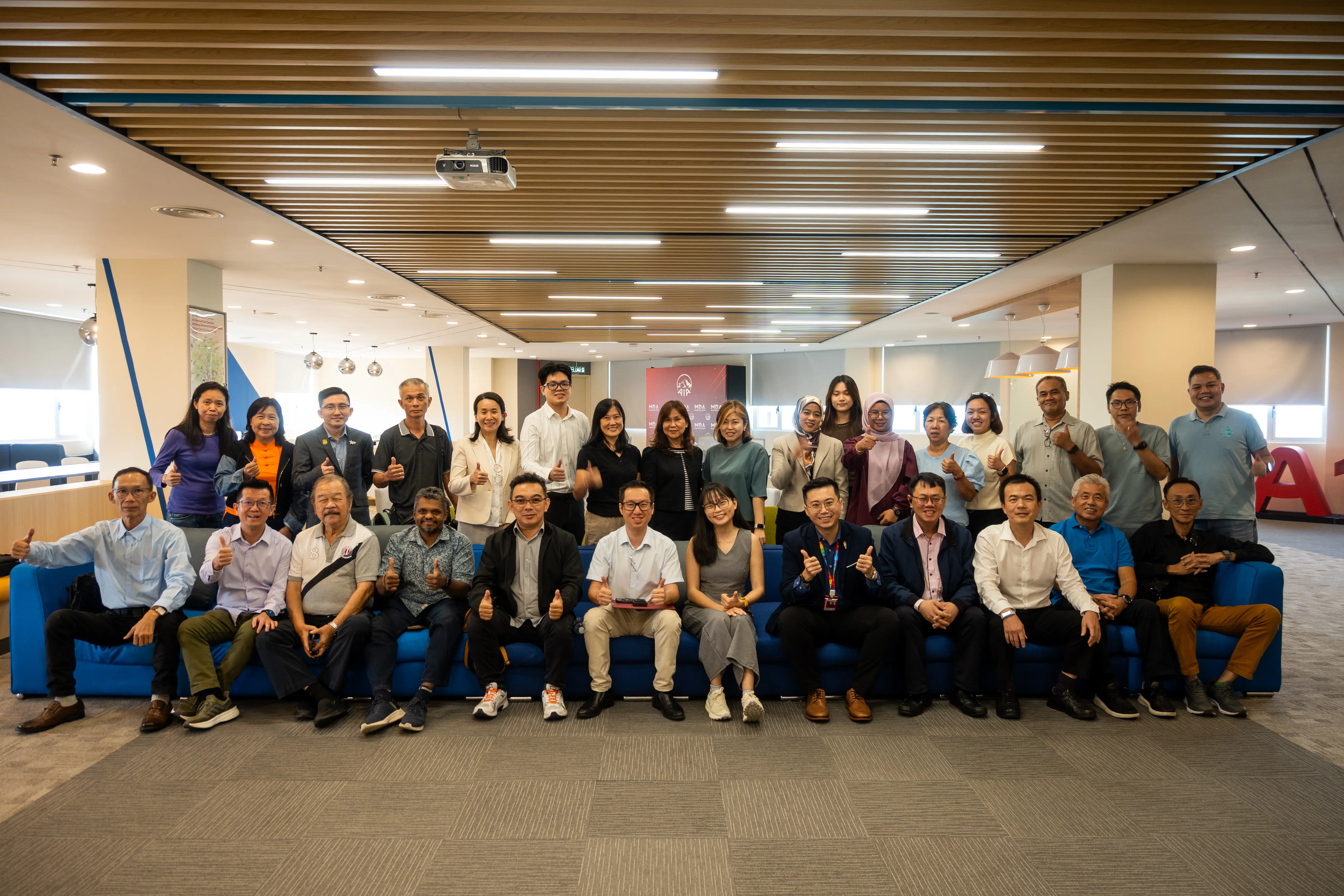 A large group of advisors and trainers seated and standing together, many giving a thumbs up, at the end of a full-day AI training session in Penang, 21 September 2026