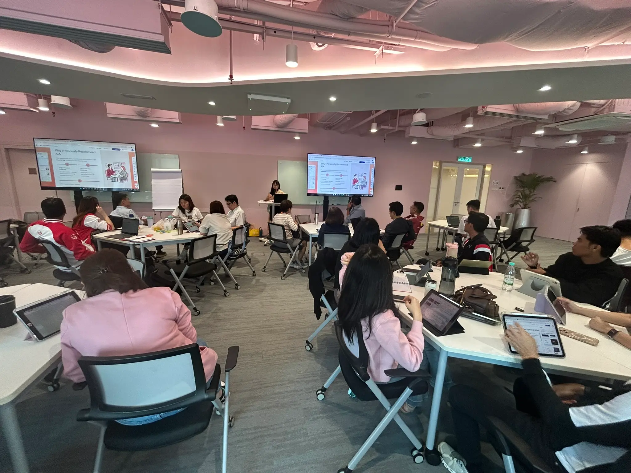 Trainer presenting an AI-generated client pitch slide, Why I Personally Recommend AIA, to advisors with tablets and laptops