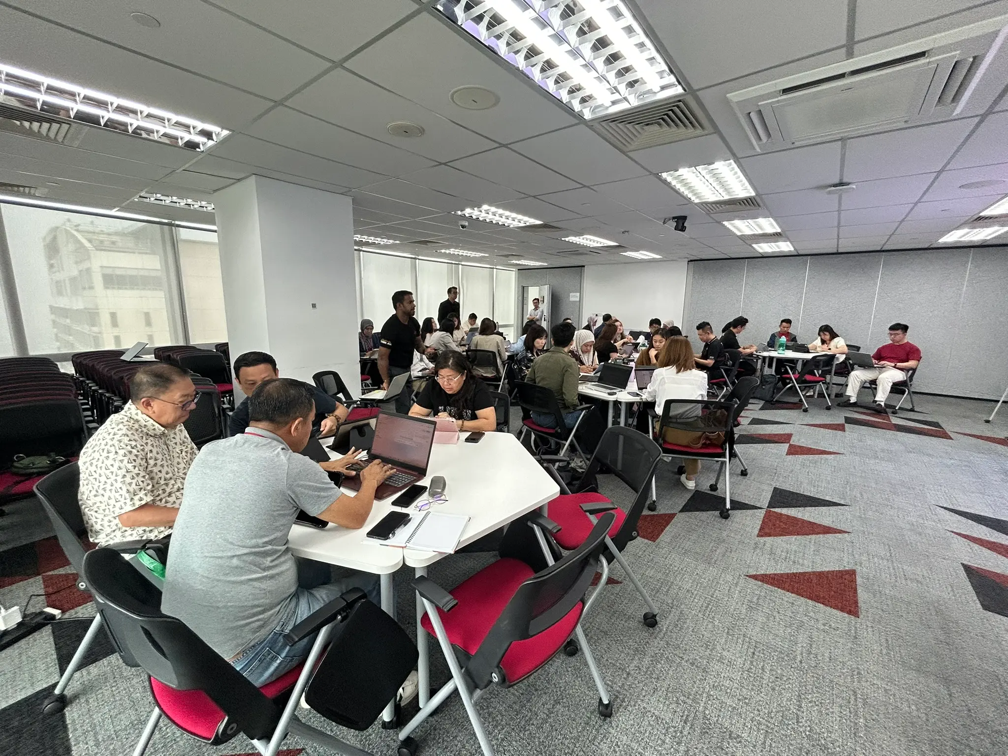 A wide training room of advisors working at tables on laptops, with a hazy view through the window, Johor Bahru, 14 October 2026