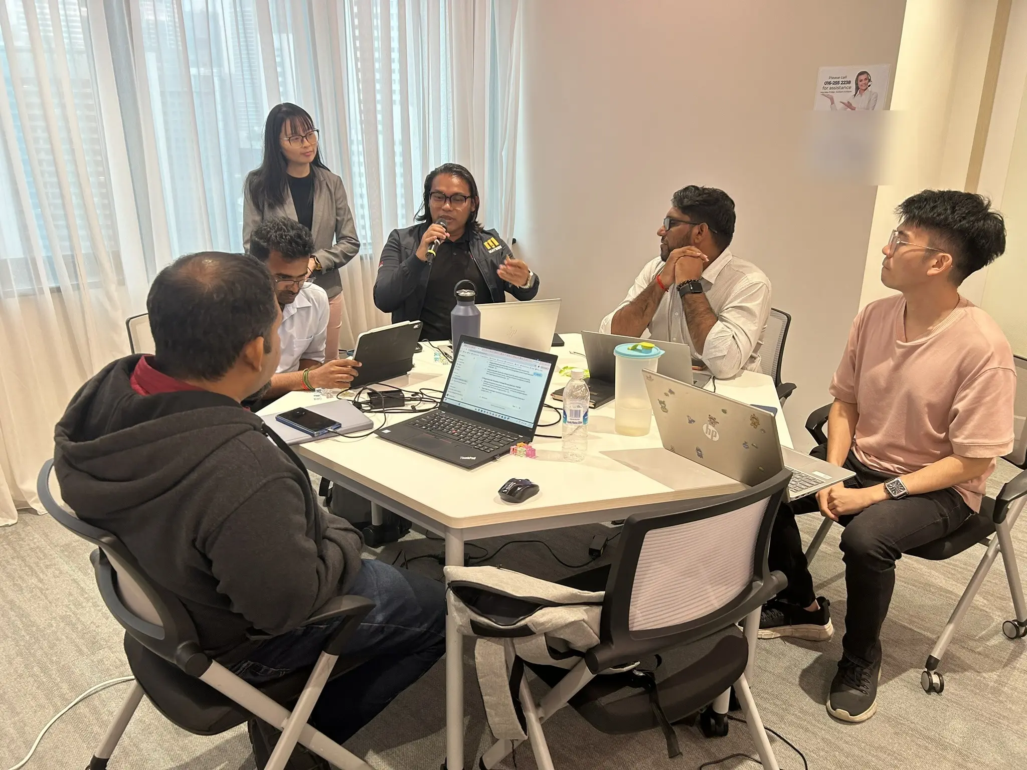 A small group of advisors in discussion around a table while one of them speaks into a microphone