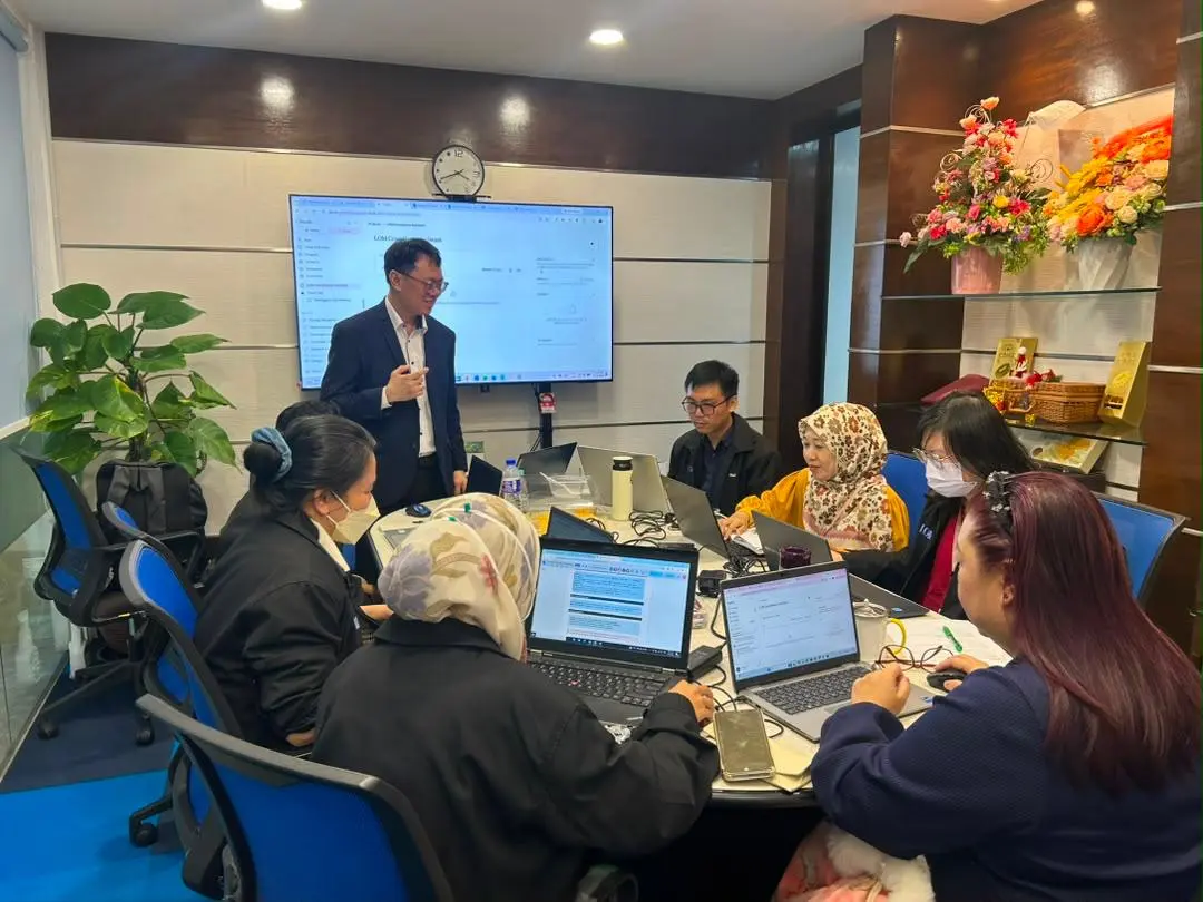 Ricky Soo presenting a compliance assistant on the screen to participants working at laptops around the boardroom table