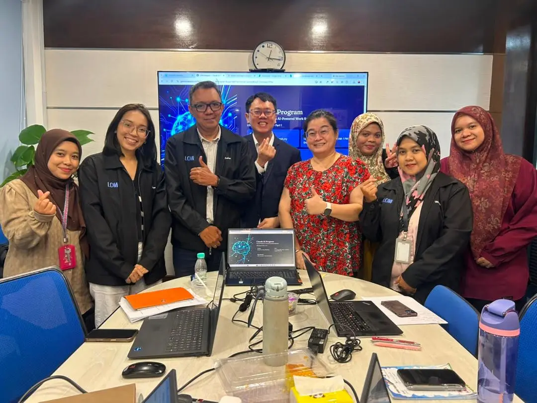 Participants and trainers gathered around the boardroom table with the Claude AI Program title slide on the screen behind them