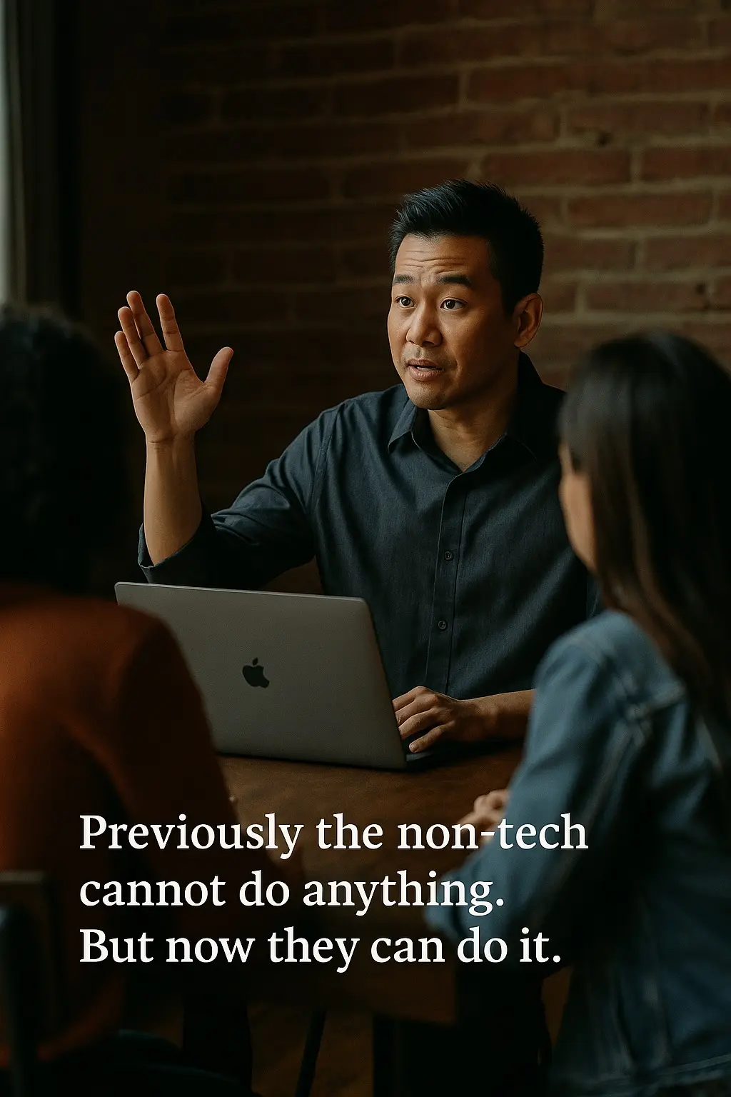 Photo of a man speaking with raised hand at a table with two others, captioned Previously the non-tech cannot do anything. But now they can do it.