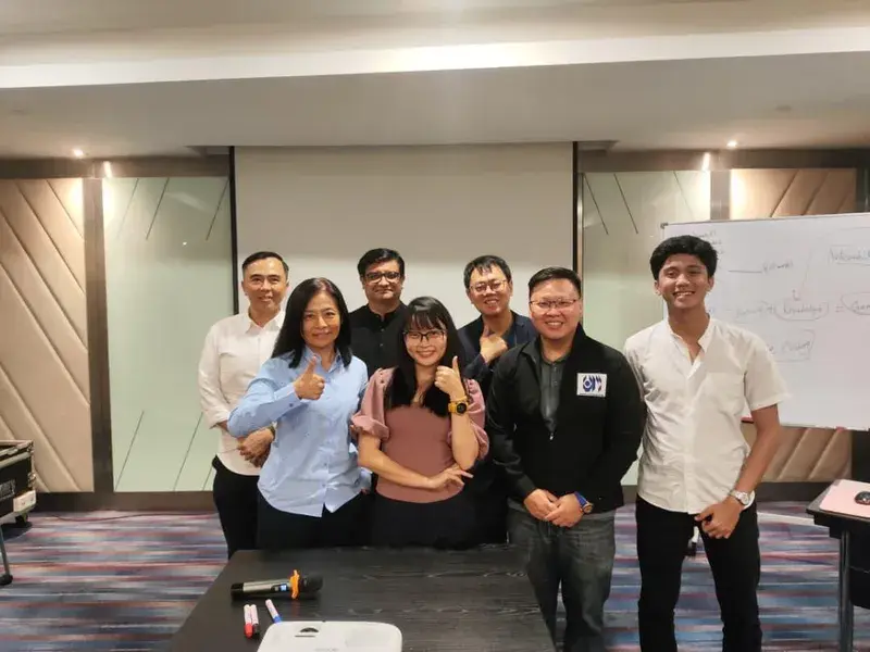 Seven participants standing together in front of a whiteboard at an AICoach.my in-person training session in Malaysia