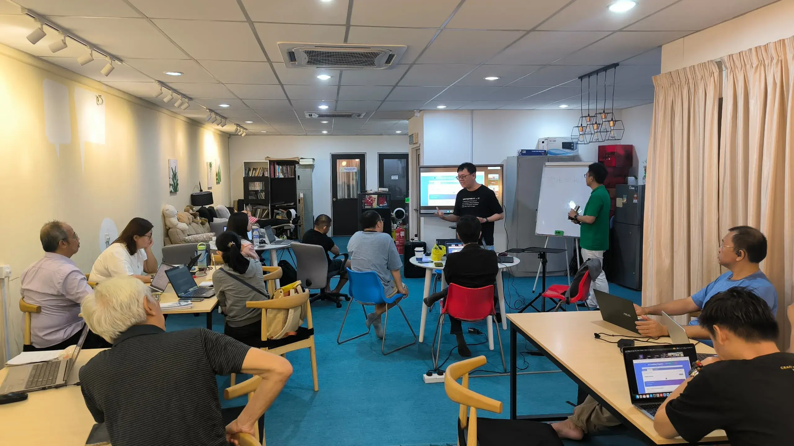 Wide view of the Inno Day #2 room with two speakers at the front and participants at laptops