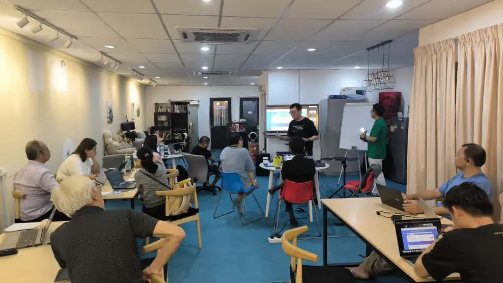 Participants seated at laptops while two speakers work at the screen and whiteboard at Inno Day #2