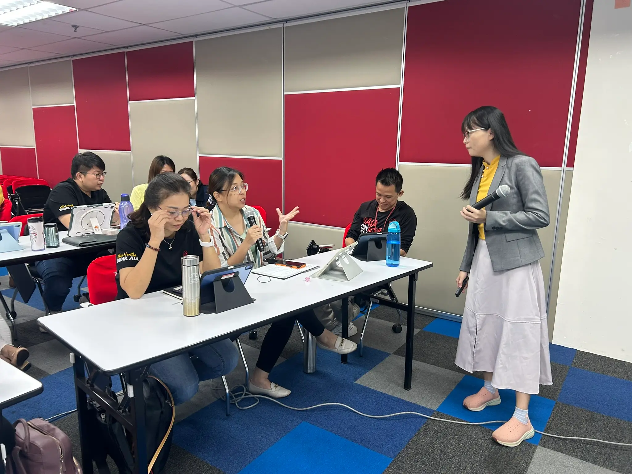几位学员围坐讨论，其中一人拿着手机分享内容，大家笑着回应