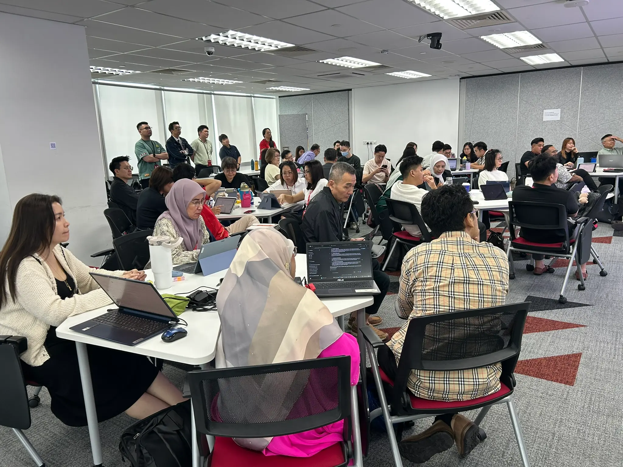 A full training room in Johor Bahru seen from the back, every table taken and several people standing along the wall