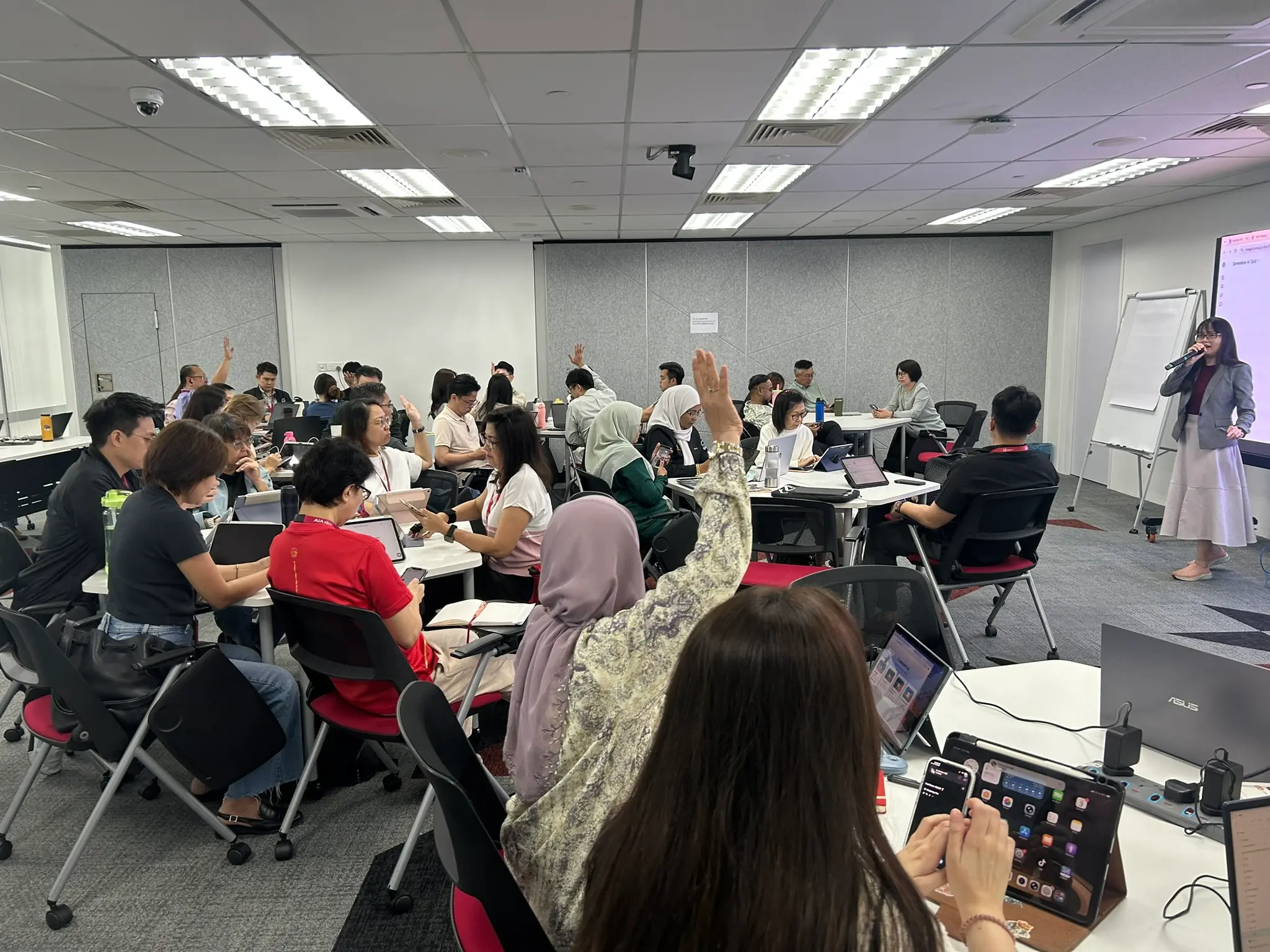 Advisors with hands raised across the Johor Bahru training room as the trainer speaks from the front