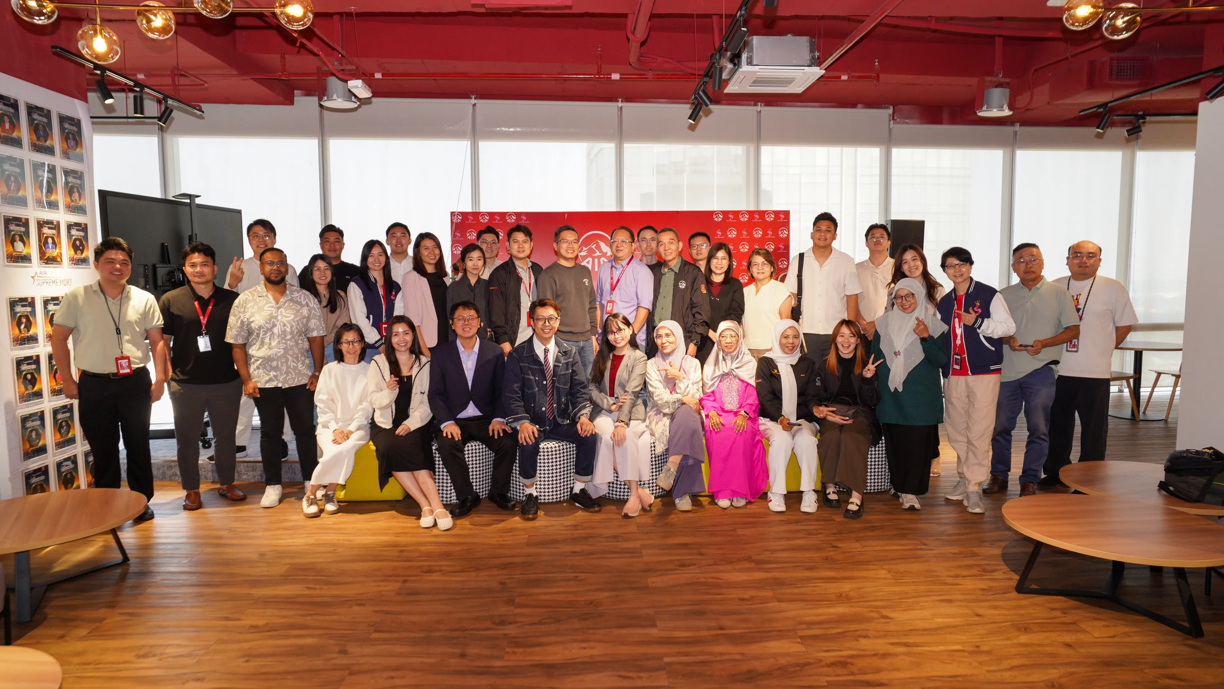 A large group photo of AIA advisors and trainers at the end of the Johor Bahru training day, in a lounge with a red backdrop, 3 September 2026