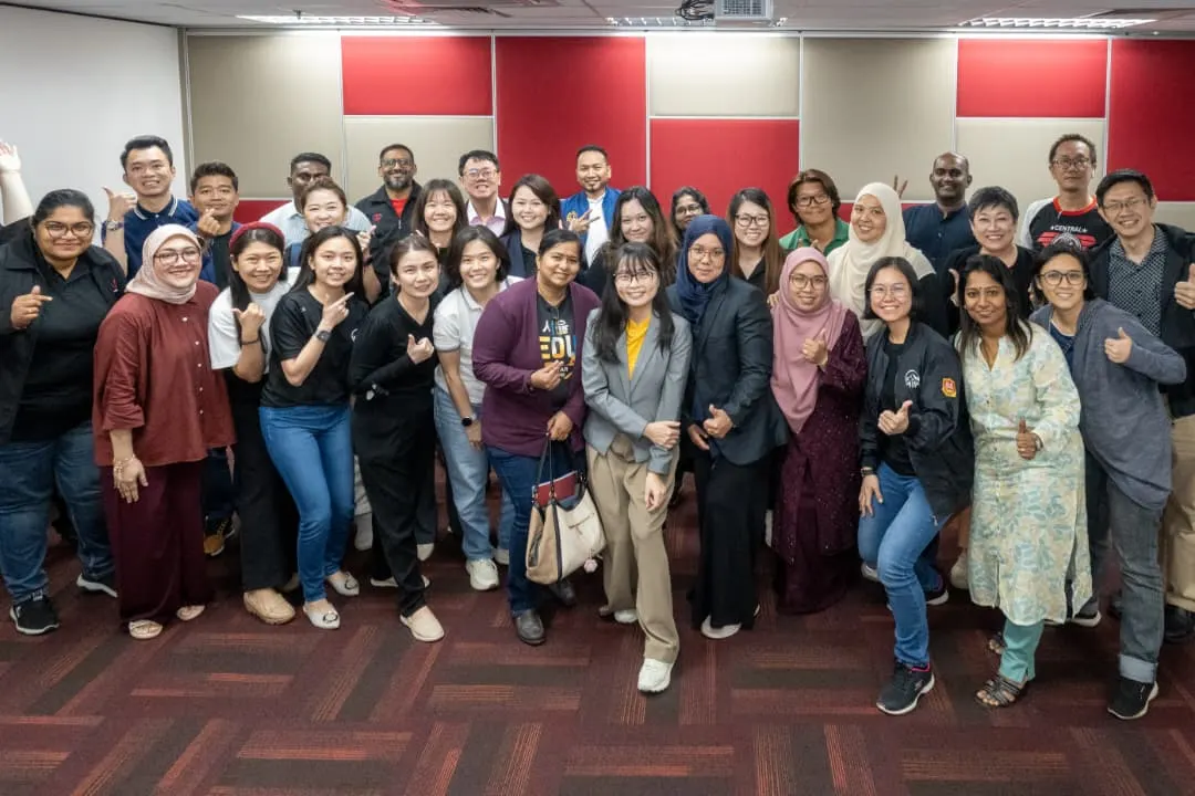 A large group of smiling advisors and trainers giving thumbs up together in a training room after a full-day AI training session in Klang, 9 October 2026