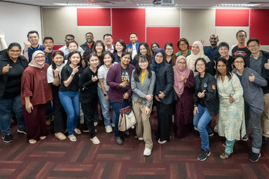 A large group of smiling advisors and trainers giving thumbs up together in a training room after a full-day AI training session in Klang, 9 October 2026