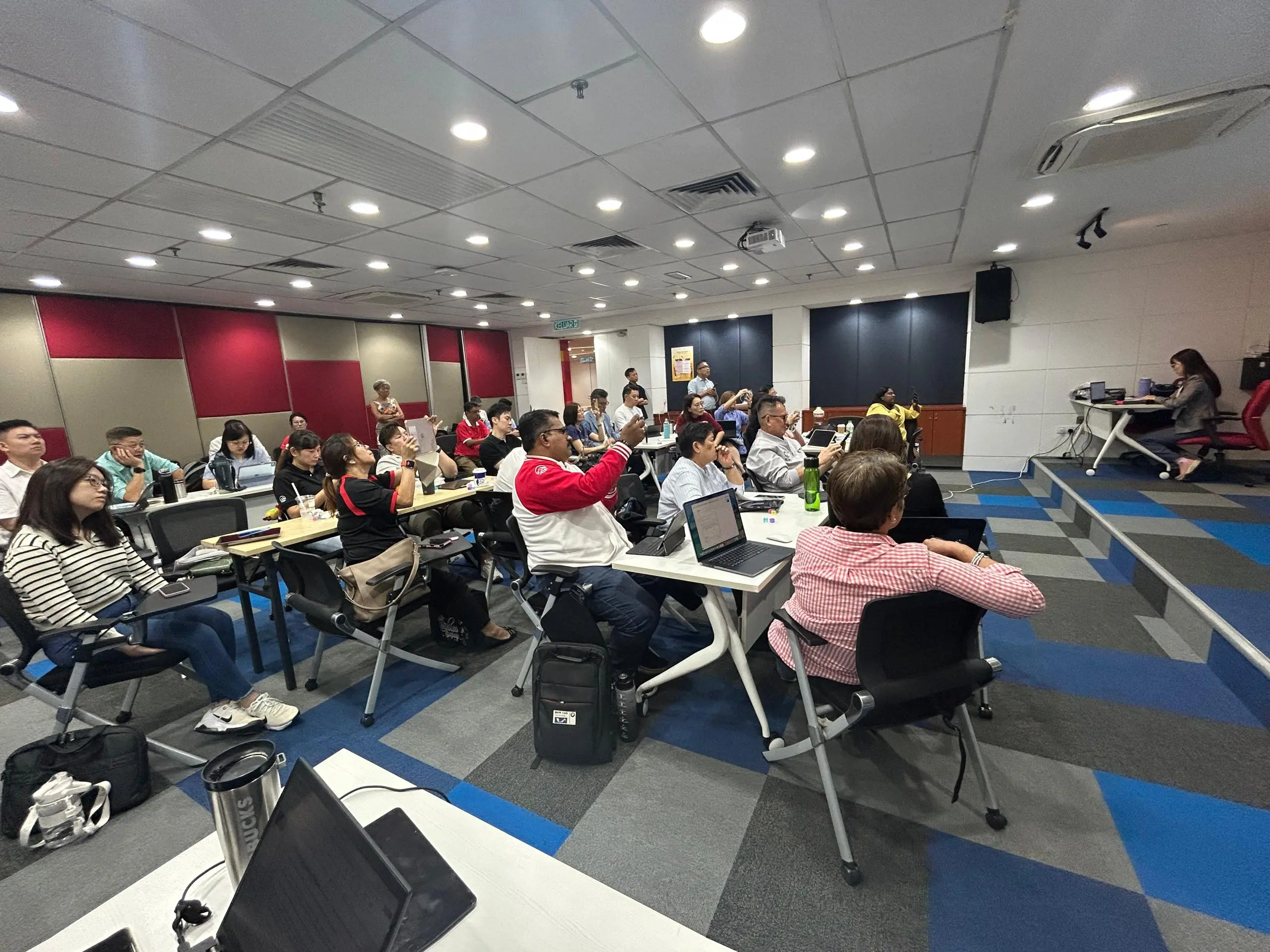 Advisors in the Klang training room raising their phones to photograph the screen as the trainer changes the slide