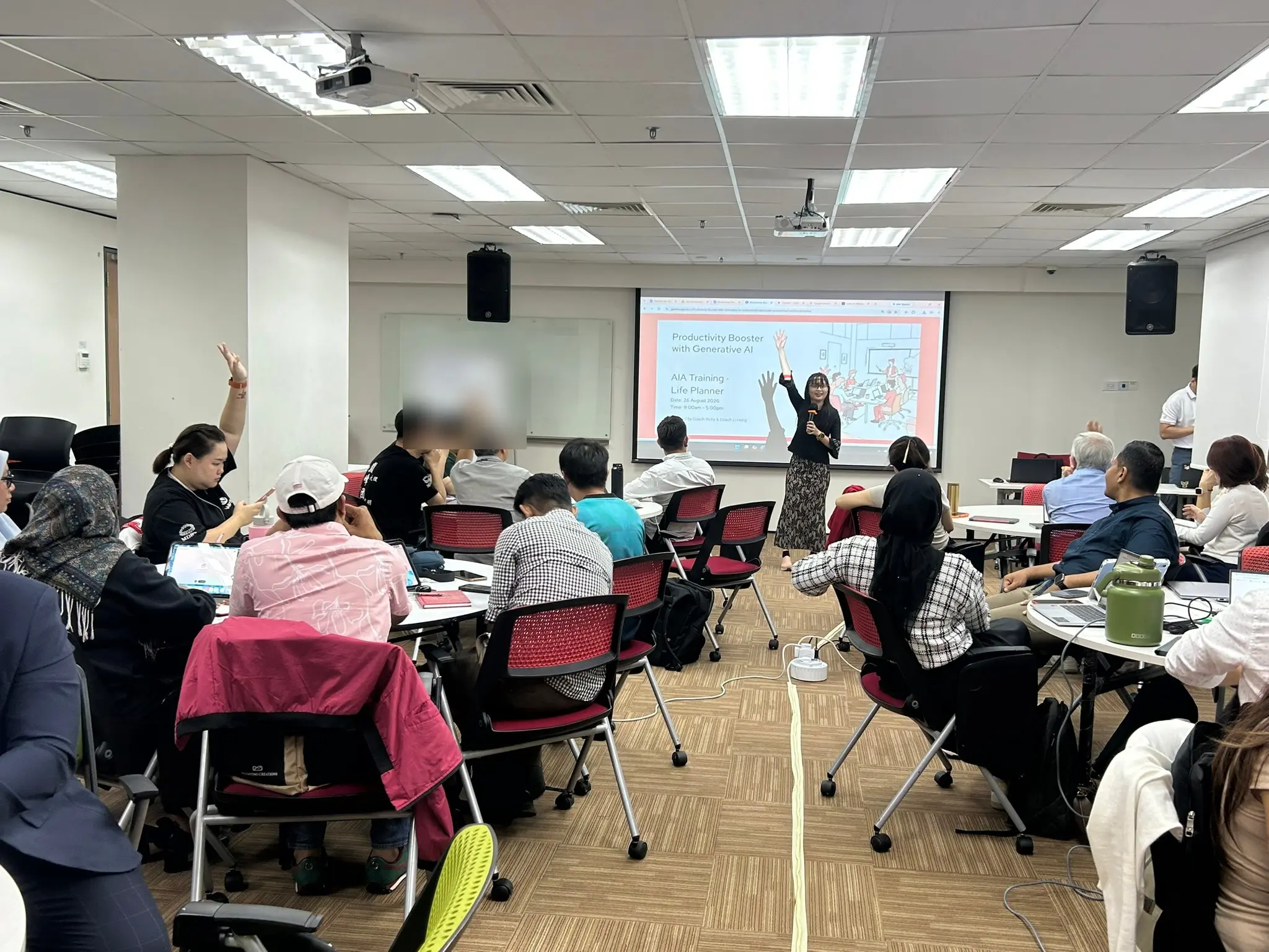 Advisors in the Kuantan training room with hands raised, seated at round tables facing the screen