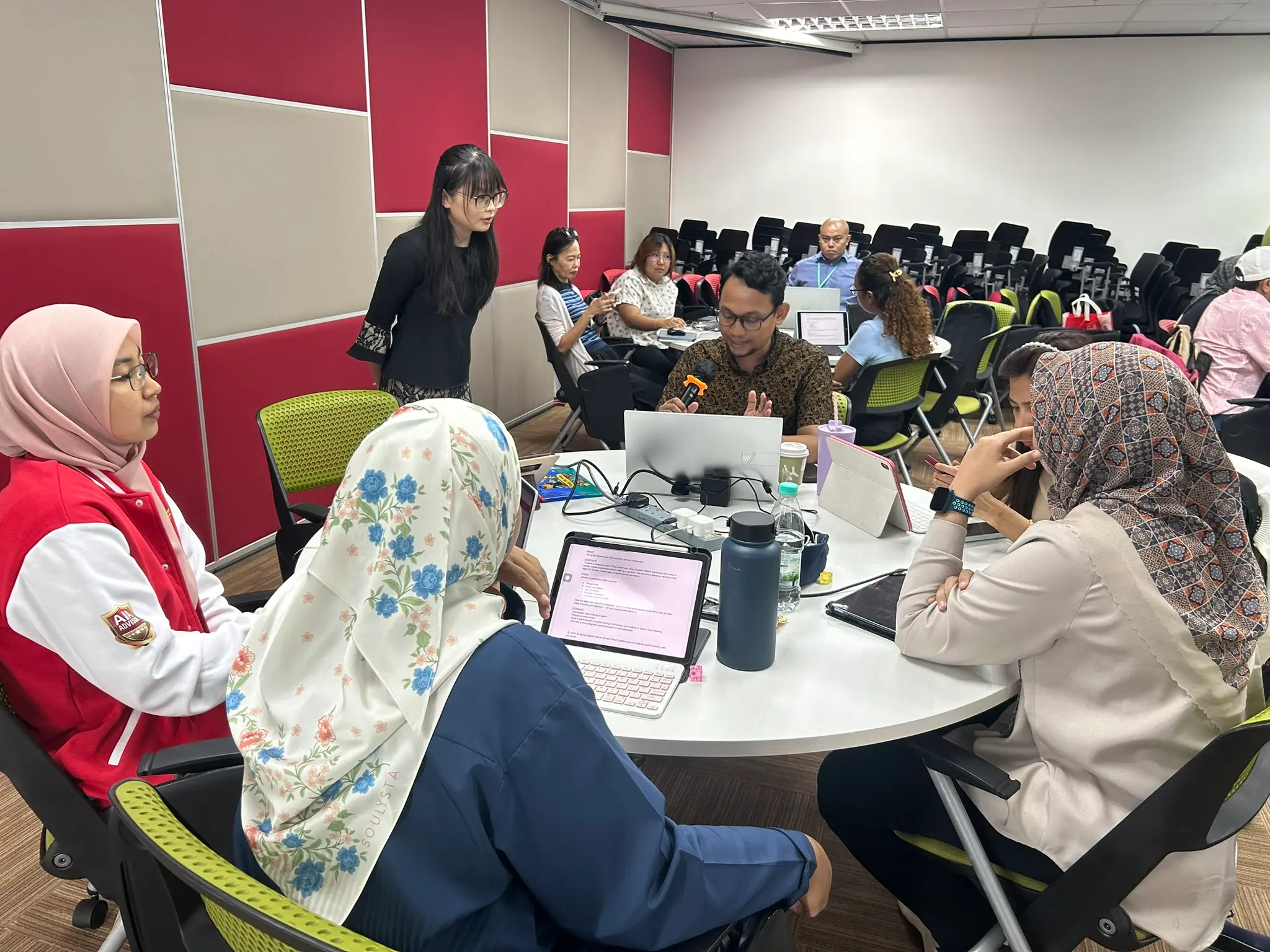 A round table of advisors working together on laptops and tablets, one of them holding the microphone
