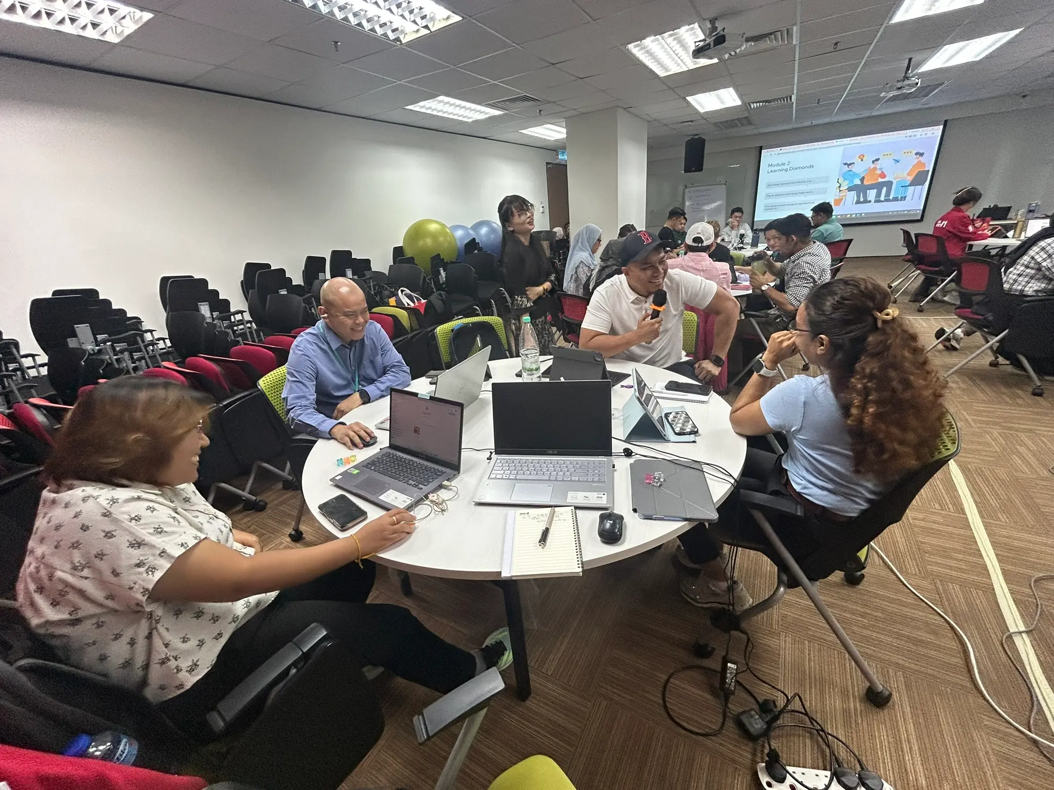 Another round table mid-discussion, with exercise balls stacked in the corner of the room behind them
