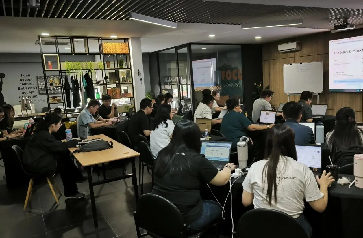 Participants working at laptops through a hands-on exercise, with the prompting framework on the screen at the front