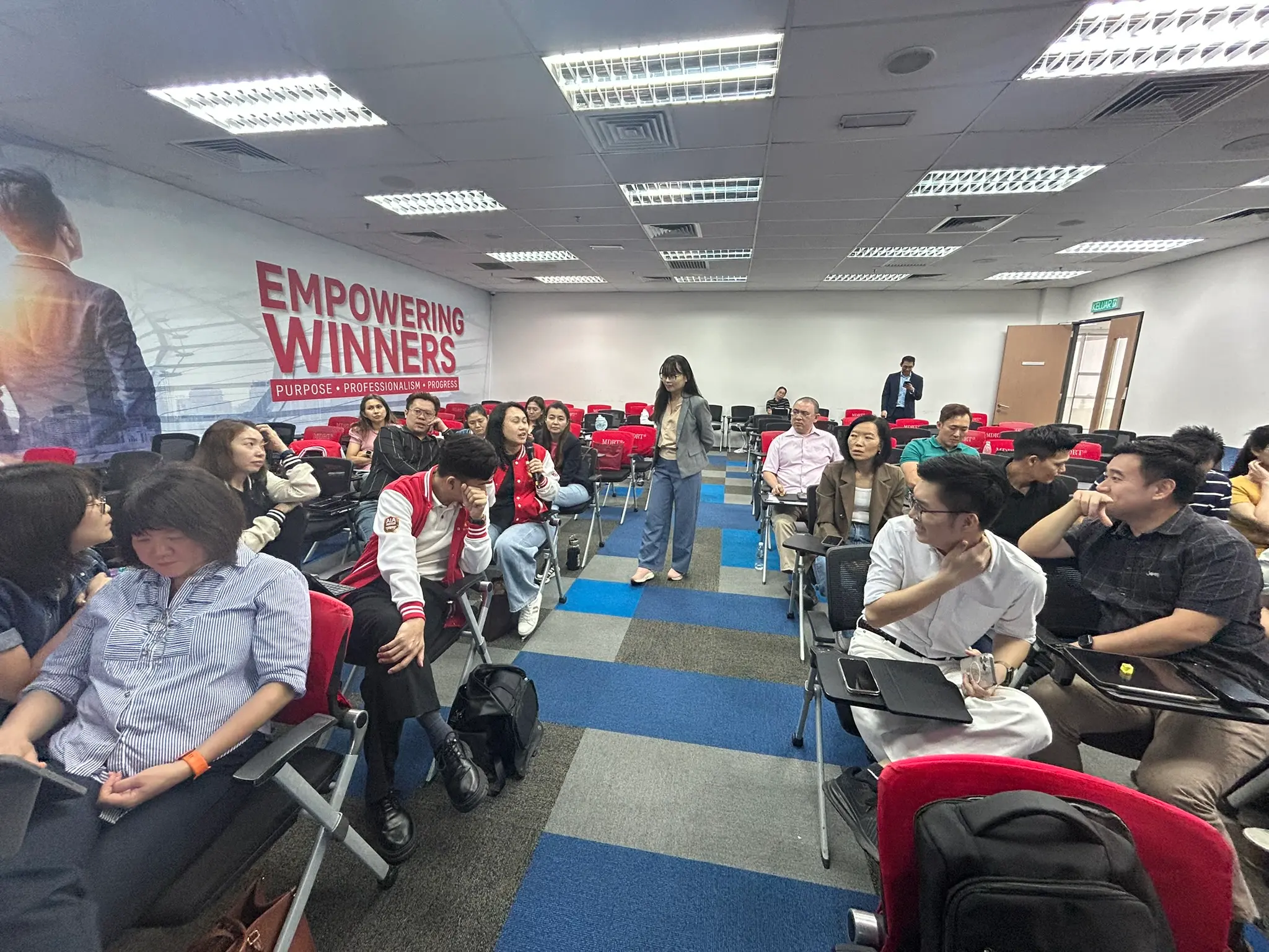 一名学员拿着麦克风站起来发言，其他人转头聆听