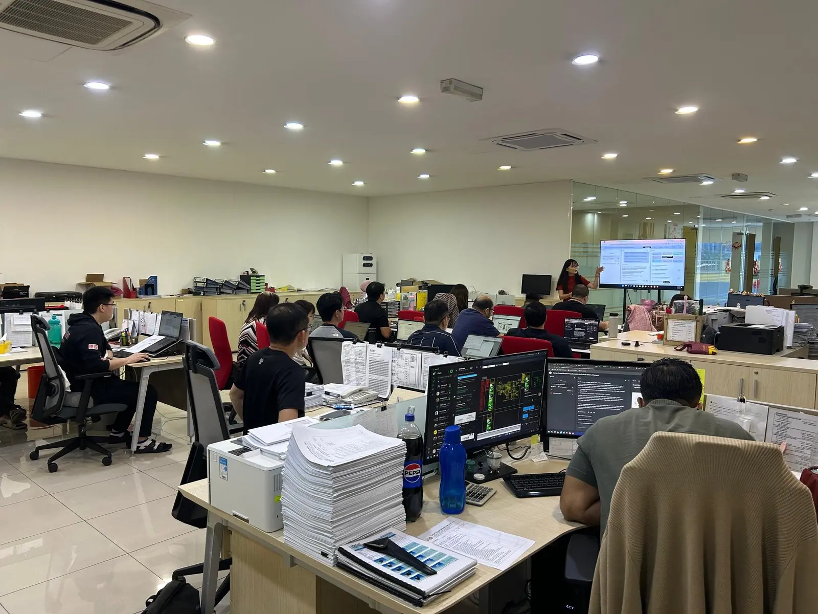 Trainer presenting from a screen wheeled into an open-plan office, with staff following along at their own desks