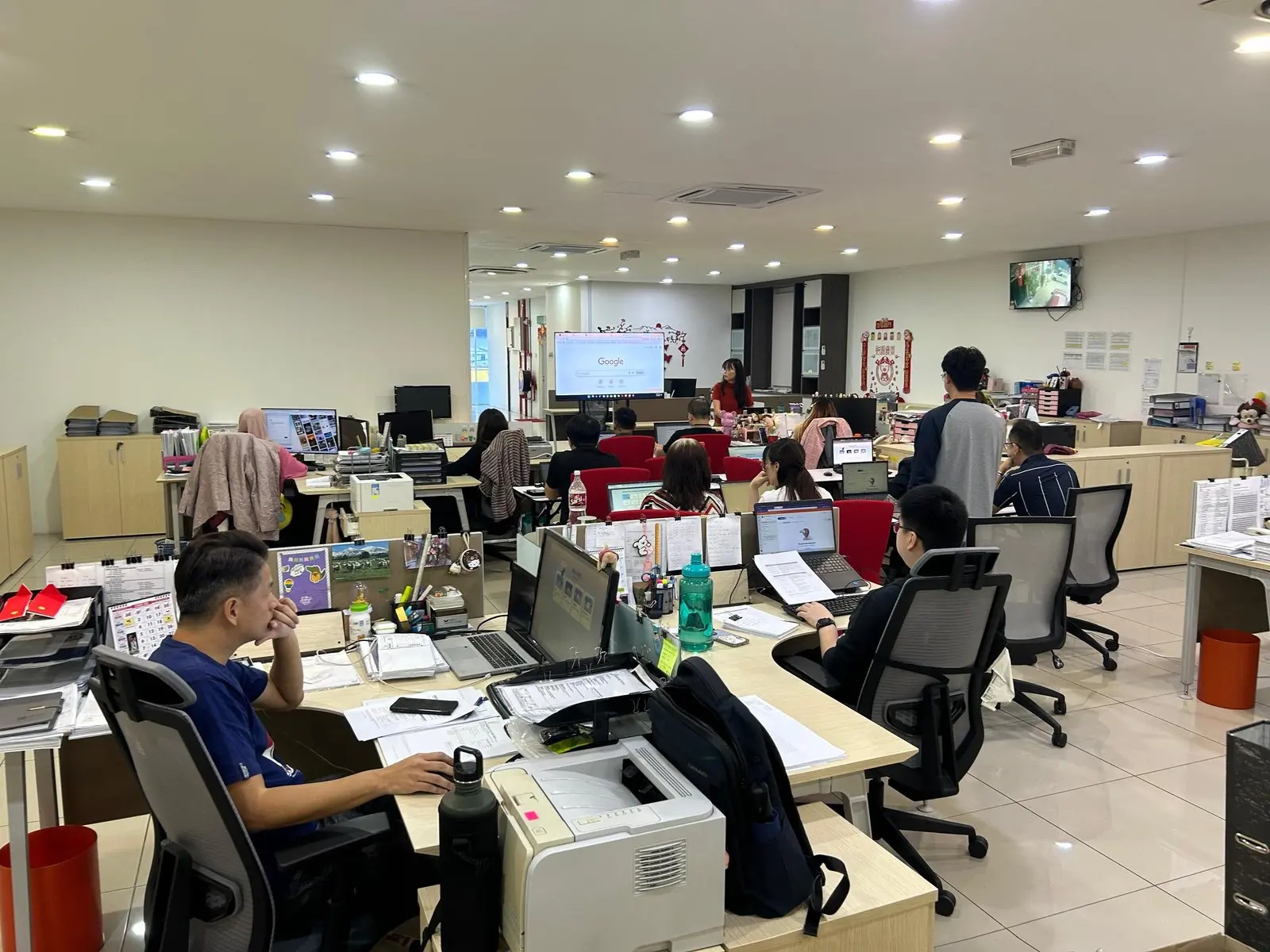 Wide view of the office during the session, rows of desks with laptops open and the training screen at the far end