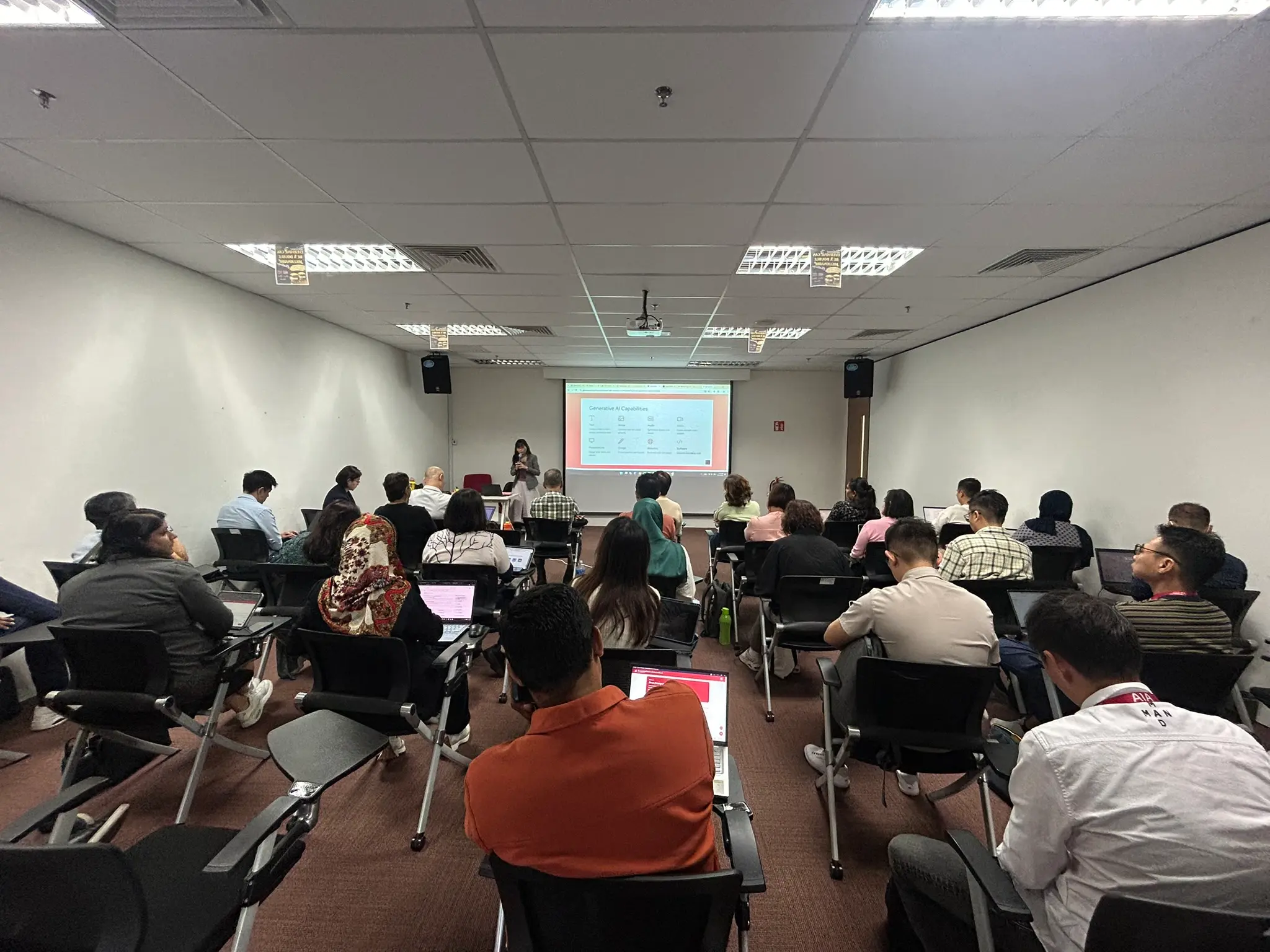 View from the back of a training room in Petaling Jaya, with rows of advisors on laptops facing a trainer and a projected screen, 23 September 2026