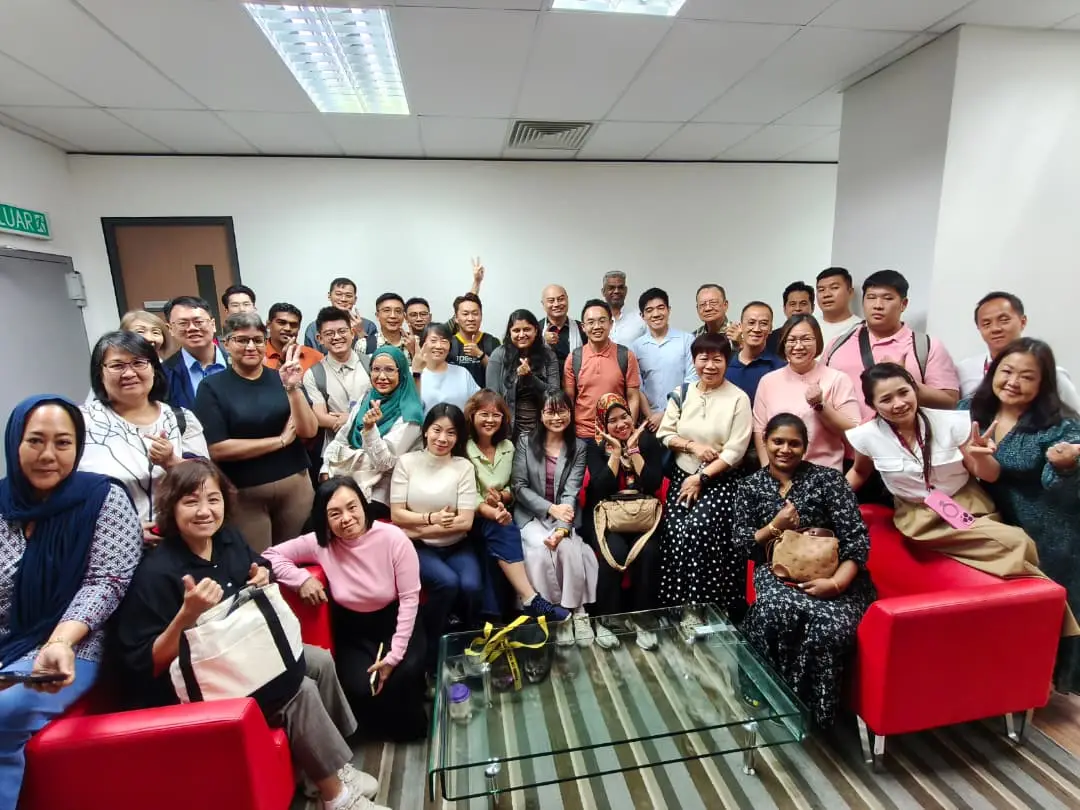 A large group of advisors and trainers crowded around red sofas and a glass coffee table for a group photo after a full-day AI training session in Petaling Jaya, 23 September 2026