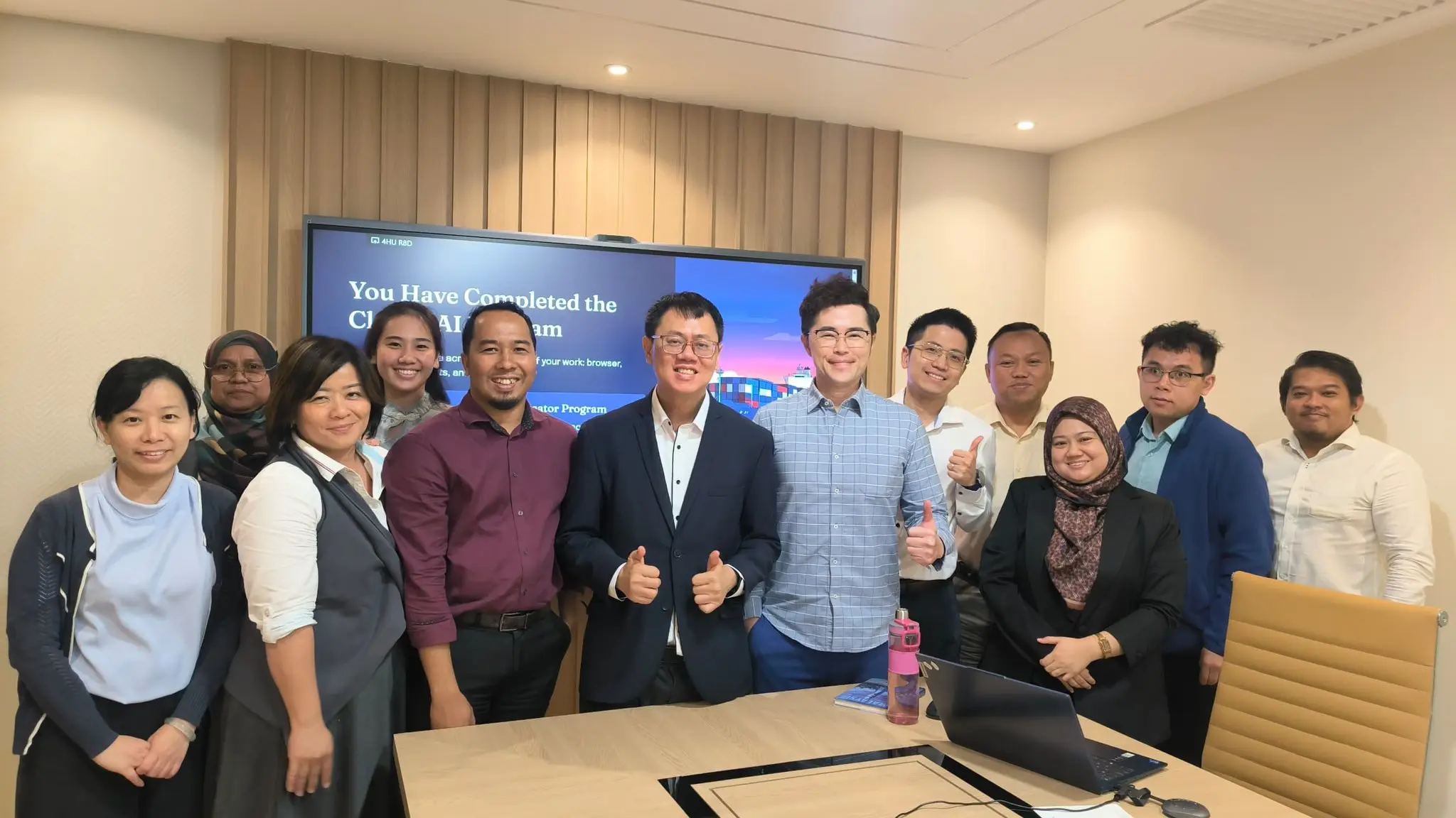 Group photo of participants standing in front of a screen reading You Have Completed the Claude AI Program