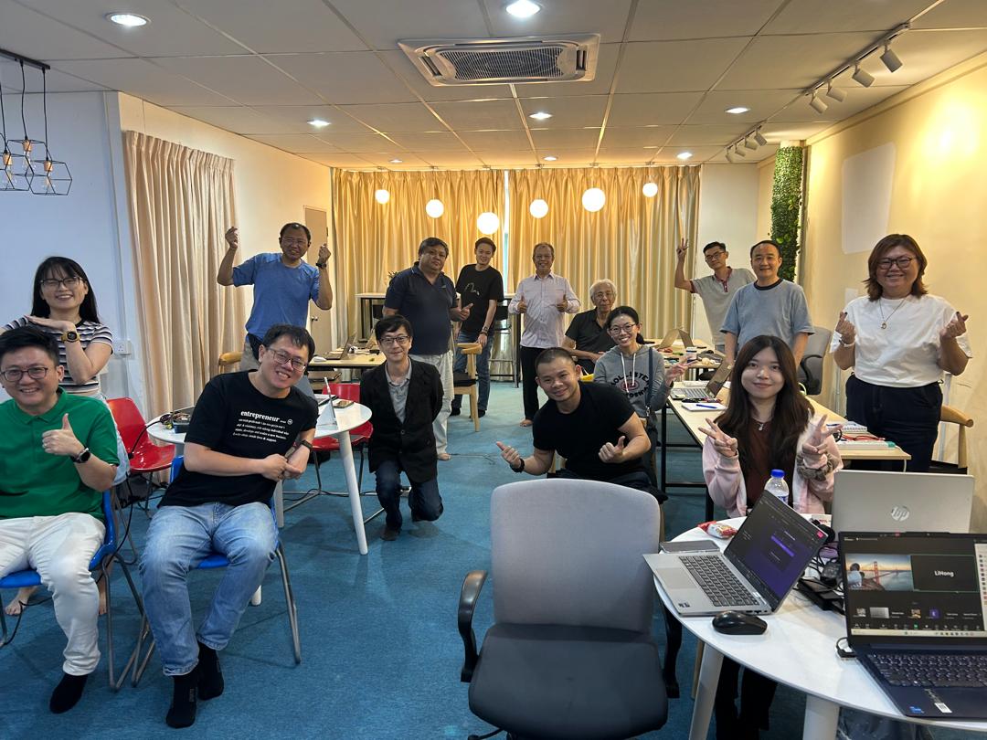 Participants posing with thumbs up in training room with laptops